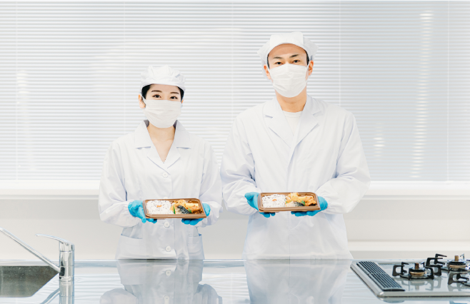 食品工場。真心込めて作った商品（お弁当）を見せる作業員の写真。